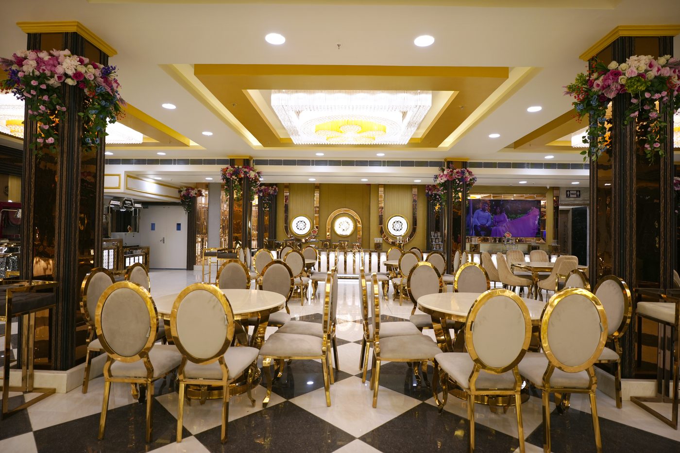 Premium gold dining tables with oval back chairs, crystal chandelier and floral pillars at The Great Palace Banquet Hall dining area