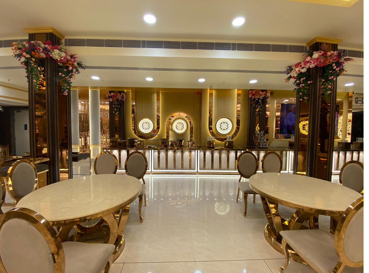 Intimate gold oval dining tables with floral pillars and illuminated backdrop at The Great Palace Banquet Hall